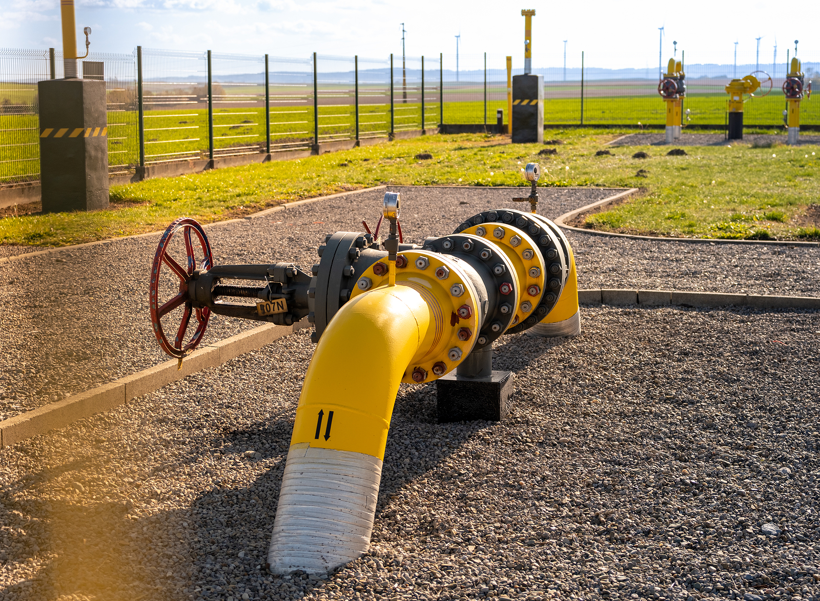 Gas pipes, natural gas transport system. Transmission infrastructure coming from the ground, yellow pipes with valve and flow meter on the background of the wind farm